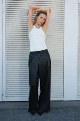Pantalón jogger negro de corte amplio, confeccionado en tejido revestido tipo cuero sintético, con cintura elástica fruncida, bolsillos laterales y bajos deshilachados.