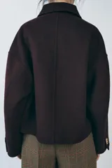 Cazadora corta color borgoña confeccionada en hilatura con lana. Tiene cuello solapa, manga larga, bolsillos delanteros y cierre frontal con botones metálicos dorados en relieve.