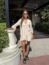 Vestido corto color beige de fibrana, con escote en V, mangas 3/4 con volados y falda con volados.