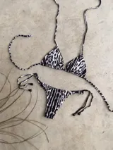 Conjunto de bikini con estampado animal print blanco y negro. El corpiño es de triángulos movibles con tiras finas para atar al cuello y a la espalda, con almohadillas desmontables. La bombacha es colaless con tiras finas para atar a los costados.