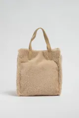 Bolso tipo tote de sherpa color beige con doble asa corta de cuero sintético.