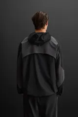 Cazadora con capucha confeccionada en tejido técnico ligero y elástico en todas las direcciones, color negro con detalles en gris. Cuenta con cuello con capucha ajustable, manga larga, bolsillos con cierre de cremallera en cadera, acabados con elástico y cierre frontal de cremallera.
