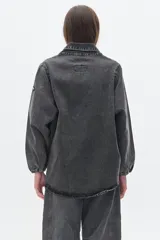 Camisa de jean oversized, color gris oscuro, con escote en V bajo, cuello camisero y mangas abullonadas. Tiene bolsillos delanteros y cierre con botones metálicos.