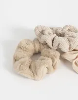 Set de tres scrunchies de pelo en tonos beige, con diferentes texturas: una de piel sintética, una de tela lisa y una tejida.