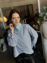 Camisa a rayas verticales azules y blancas, de popelina de algodón, con cuello verde y botones marmolados. Es corta adelante y larga atrás.