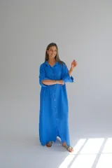 Camisola larga azul francia de lino italiano, con cuello camisero, mangas largas con puños abotonados, cierre frontal con botones y bolsillos de parche en el pecho.