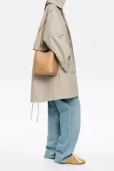 Bolso tote pequeño de piel reconstituida color gris claro, con estructura rígida, doble asa corta, correa extraíble, cierre con botón de presión, logo metálico BIMBA Y LOLA, acabados metálicos, bolsillo interior con cierre de cremallera e interior con logo grabado.