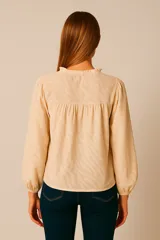 Blusa color crema con estampado de cebra, cuello mao con volantes y lazo, mangas largas abullonadas con puños elásticos.