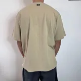 Remera color arena de corte oversize, con cuello redondo y mangas cortas. Presenta un pequeño bordado de un sol naciente en el centro del pecho.