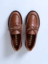 Mocasín de cuero color marrón claro, con cordones y detalle de costuras en la puntera.