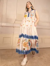 Vestido largo color crema con estampado de flores y corazones en tonos azules, naranjas y amarillos. Tiene cuello en V con ribete azul y corte imperio con falda escalonada.