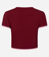 Remera deportiva cropped de manga corta, color rojo oscuro, con cuello redondo y ribetes contrastantes en blanco en el cuello y los puños. Presenta una pequeña inscripción en el pecho.