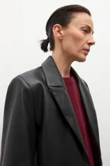 Blazer de mujer color negro, confeccionado en eco cuero, con solapas anchas, cierre frontal de un solo botón y pespuntes visibles.