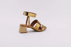 Sandalias plateadas con dos tiras horizontales sobre el pie y una tira vertical que se une a una pulsera con hebilla en el tobillo. La pulsera tiene ojales y tachas combinadas. El taco es cuadrado y de 5 cm.