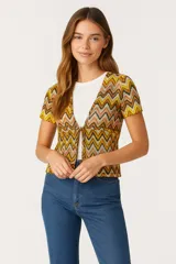 Top tejido de poliéster con estampado de zigzag en tonos amarillo, naranja, marrón y blanco. Tiene escote en V, mangas cortas y se anuda en el frente.