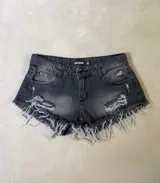 Short de jean negro con efecto gastado, tiro alto, corte ajustado, roturas y terminaciones desflecadas.