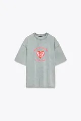 Camiseta rosa de algodón con efecto lavado, corte regular, cuello redondo y mangas cortas. Estampado frontal con la frase "Puerto Rico Vuela Conmigo".