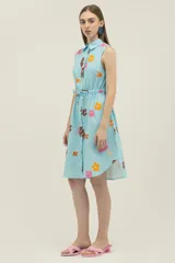 Vestido camisero celeste con estampado de flores de colores, confeccionado en tejido seersucker de algodón con elastano. Tiene cuello camisero, botones nacarados, lazo para ajustar la cintura con terminación en cobre y bolsillos laterales.