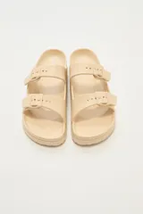 Sandalias planas color beige con doble tira y hebillas ajustables.