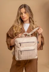 Mochila mediana color beige de símil cuero con asa superior, dos compartimentos con cierre, bolsillos frontales y tiras ajustables.