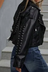 Campera negra de cuero sintético estilo biker con cierre cruzado, cuello con solapas y detalle de cordones con ojalillos metálicos en las mangas.