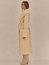 Abrigo trench maxi color beige con ribete de piel sintética en cuello y puños.