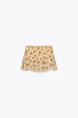 Minifalda color crema con estampado floral en tonos rojos y verdes. Presenta volados con puntilla en el ruedo.