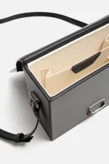 Bandolera rígida negra en formato caja con cierre metálico y asa de hombro ajustable.