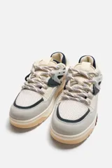 Zapatilla urbana de cordones con capellada de cuero sintético y malla en tonos beige, gris, azul marino y bordó. Suela de goma color caramelo con detalles en bordó.