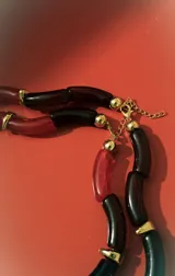 Collar de dos vueltas con eslabones tubulares curvos, alternando colores negro y rojo translúcido, separados por pequeños detalles metálicos dorados.