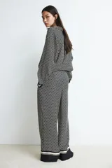 Pantalón de tiro alto con elástico en la parte posterior de la cintura y cierre oculto lateral. Presenta bolsillos discretos en las costuras laterales y piernas anchas con pliegues adelante y atrás. Diseño estampado con motivos geométricos en blanco y negro.