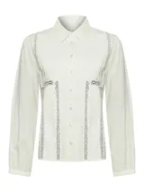 Blusa color crema con cuello camisero, mangas largas y detalles de encaje en el frente.