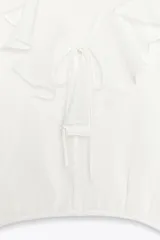 Blusa color marrón con escote en pico, manga larga abullonada con elástico en los puños y volantes en el escote y mangas.