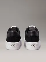 Zapatillas de ante negras con plataforma blanca y logo CK en el lateral.