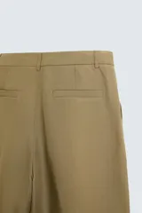 Pantalón color caqui de corte amplio, confeccionado en tejido de lyocell y lino. Presenta pliegues frontales, bolsillos laterales y traseros de ojal. Cierre frontal con cremallera y botón.