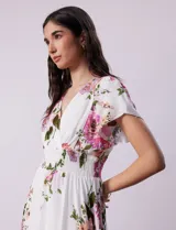 Vestido blanco con estampado floral en tonos rosados, violetas y verdes. Escote en V tanto en la parte delantera como en la espalda. Cintura elastizada con punto smock y forro interno a tono.