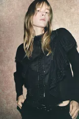 Blusa negra de viscosa con cuello perkins y manga larga. Detalles de bordados, lentejuelas y volantes. Cierre en la espalda con abertura y botones.