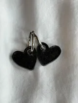 Aros colgantes con forma de corazón, hechos de acrílico negro y con cierre de aro plateado.
