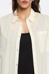 Camisa blanca con rayas verticales amarillas, de corte recto, manga larga con puños abotonados, cuello camisero y bolsillo de parche en el pecho.