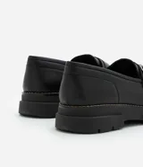 Zapato negro de cuero sintético con punta redonda, detalle de hebilla plateada y suela track.