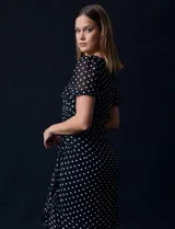 Vestido midi de gasa color negro con lunares blancos, con mangas cortas, escote redondo y ruedo asimétrico. Presenta un frunce lateral con lazo de ajuste.