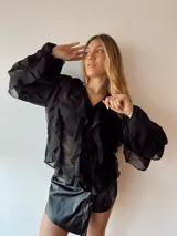 Blusa negra traslúcida con volados y mangas largas abullonadas.