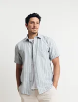 Camisa de manga corta a rayas verticales en tonos celeste, verde y blanco, con cuello clásico y bolsillo en el pecho. Cierre frontal con botones. Corte recto.