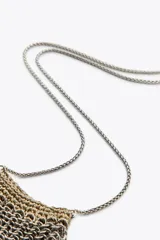 Bolso mini tipo saco confeccionado con hilo metalizado y arandelas en forma de malla. Detalle de aplicaciones metálicas de diferentes formas. Asa tipo cordón metálico.