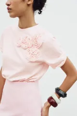 Camiseta blanca de algodón de manga corta y cuello redondo con detalle de flores en relieve en el frente.