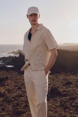 Camisa de manga corta color beige claro, confeccionada en mezcla de lino y algodón. Tiene cuello abierto, tapeta lisa, bolsillo superior abierto, canesú en la espalda y bajo recto con aberturas laterales.