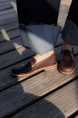 Mocasines de cuero marrón con diseño de cocodrilo, suela plana y detalle de antifaz en el empeine.