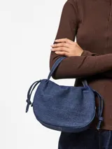 Bolso tipo bombonera confeccionado en denim azul, con asa superior y correa ajustable y desmontable.