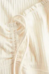 Vestido corto color crema, de punto acanalado, con escote corazón ribeteado en encaje y cordón para ajustar en el centro del busto. Modelo de manga corta con cuerpo entallado y falda con vuelo.