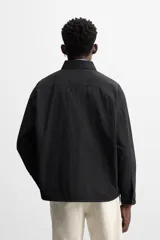 Sobrecamisa color crema de tejido técnico ligero, corte regular fit, cuello solapa, manga larga con puños abotonados, bajo ajustable con elástico en laterales y cierre frontal con cremallera.